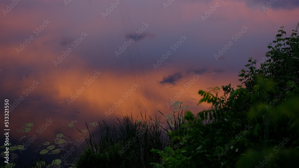 Cloudscape in summer at sunset on the lake and field