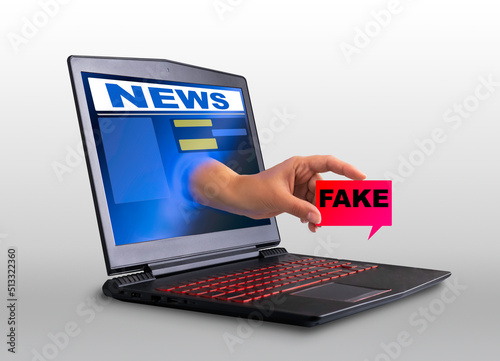 A hand sticks out of the laptop screen and holds a sign that says fake, a concept of propaganda and advertising on the Internet. creative composition,
