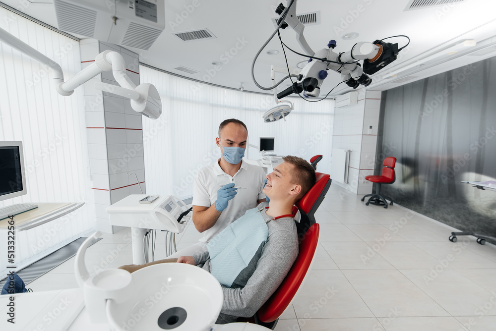 Fototapeta premium A young dentist examines and treats the teeth of a young man in modern white dentistry close-up. Dental prosthetics, treatment and teeth whitening. Modern dentistry. Prevention.