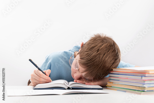 Bored and tired boy doing homework on desk. Schoolboy fell asleep on notebook. Home schooling.