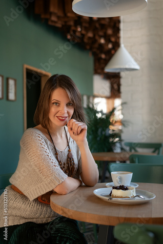 Smiling middle-aged woman in boho clothes with wooden beads rest in cafe. Woman with coffee and dessert in cafe © somemeans