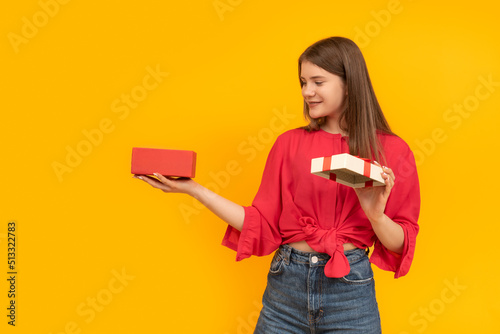 Happy young woman with an open gift box and looks into it. Smiling girl received gift. Yellow background.
