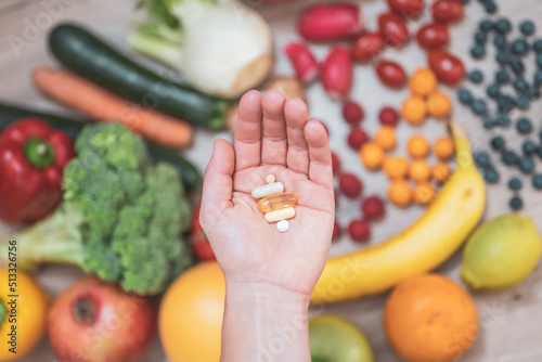 Hand holding food supplements over vegetables and fruits for a healty lifestyle photo