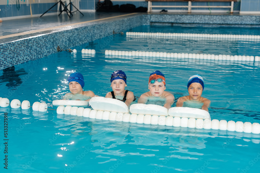 Boys and a girl play together and learn to swim in a modern swimming pool. Learn to swim. Development of children's sports. Healthy parenting and promotion of children's sports.