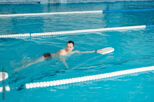 A group of boys and girls train and learn to swim in a modern swimming pool with an instructor. Development of children's sports. Healthy parenting and promotion of children's sports. © Andrii