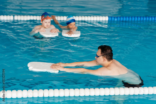 A group of boys and girls train and learn to swim in a modern swimming pool with an instructor. Development of children's sports. Healthy parenting and promotion of children's sports.