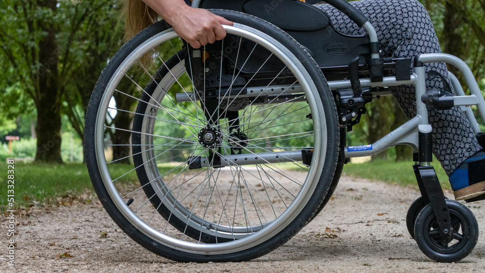 Close-up of a wheelchair in profile, a young woman sitting on it, in the middle of nature