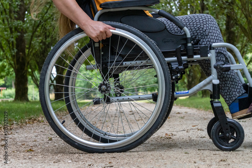 Close-up of a wheelchair in profile, a young woman sitting on it, in the middle of nature