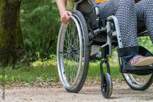 Close-up of a wheelchair from the front, a young woman sitting on it, in nature
