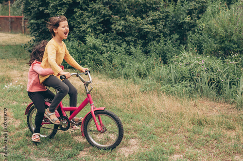 Two caucasian girls friends rides a bike through the countryside, care and sisterly love, Ukrainian children and village photo