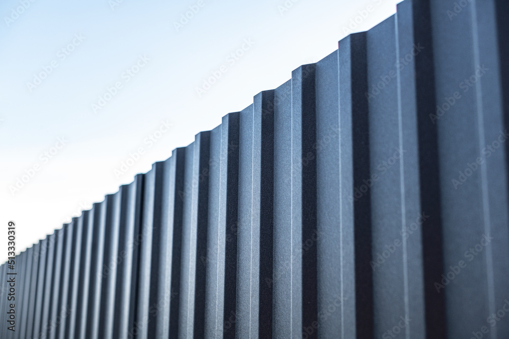 Obraz premium Iron fence and blue sky. A fence from a profiled sheet against the sky with white clouds.