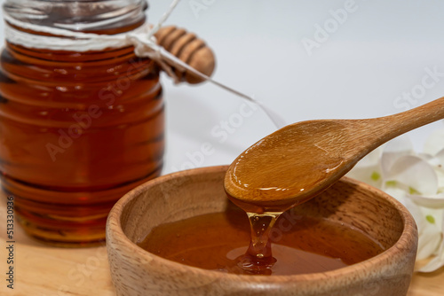 fresh pure honey in glass bowl with honey dripper on wooden tray.