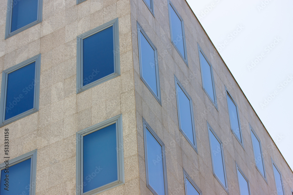 A corner of modern concrete gray high rise office building with many glass windows in business center, neighborhood, city district. Skyscrapers in the urban space. Corporate buildings exterior facade. A corner of modern concrete gray high rise office building with many glass windows in business center, neighborhood, city district. Skyscrapers in the urban space. Corporate buildings exterior facade.