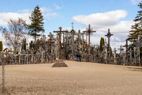 Hill of crosses near Šiauliai, Lithuania in cloudy spring day. Wooden Catholic crosses on the hill and two people from back near these. Religious pilgrimate place in Lithuania. photo