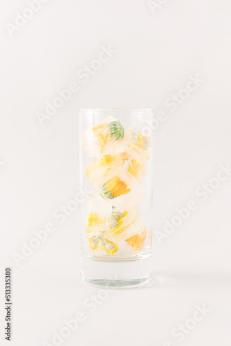 A creative arrangement made of a glass and an iced drink with flowers. Minimal summer and refreshment concept on a gray background.