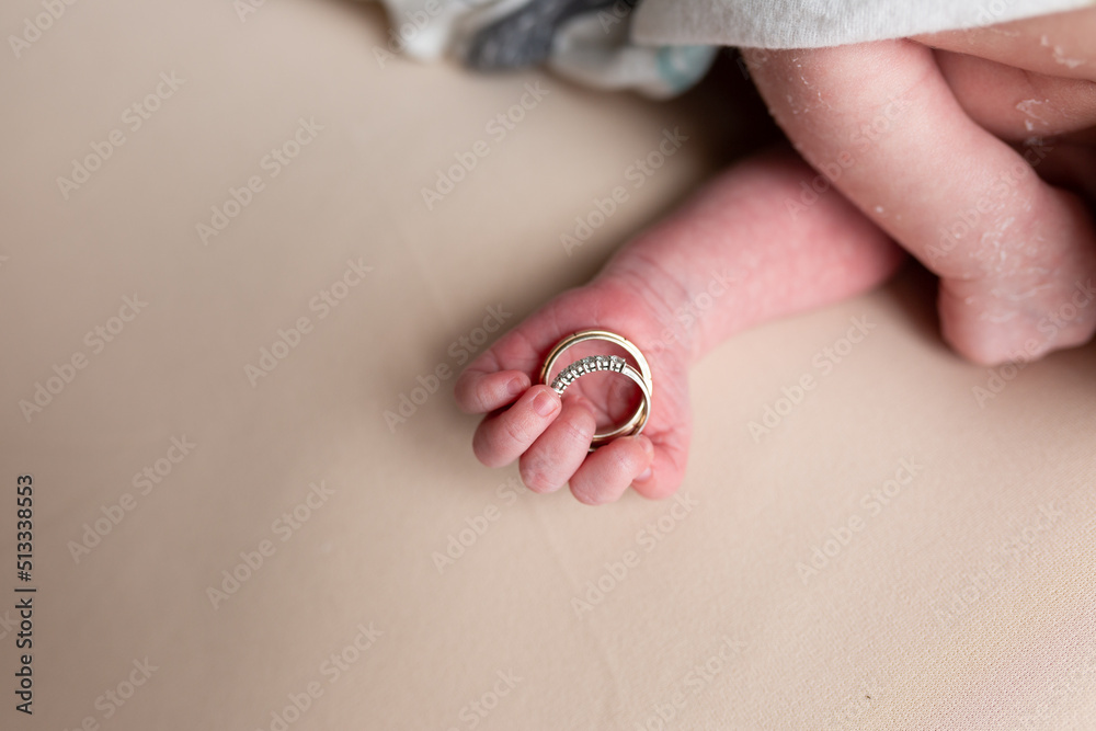 hand of a newborn with wedding rings of parents. small pens. hands on a white background. ring in a child's hand