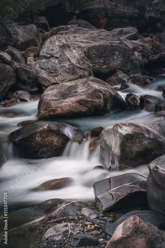 Atmosphärischer Naturhintergrund mit riesigen Steinen im Bergfluss. Große Felsen im mächtigen Wasserstrom, Nahaufnahme. Naturhintergrund mit Wald. Dunkel türkisblauer Fluss mit Steinen.