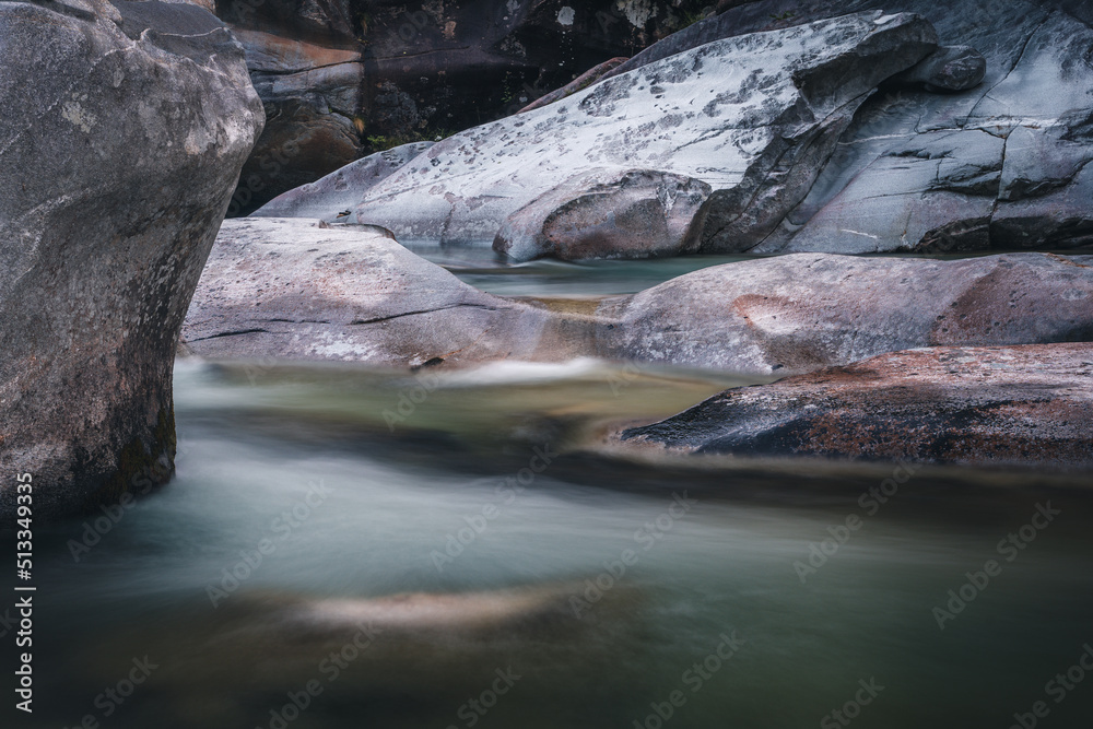 Fototapeta premium Atmosphärischer Naturhintergrund mit riesigen Steinen im Bergfluss. Große Felsen im mächtigen Wasserstrom, Nahaufnahme. Naturhintergrund mit Wald. Dunkel türkisblauer Fluss mit Steinen.