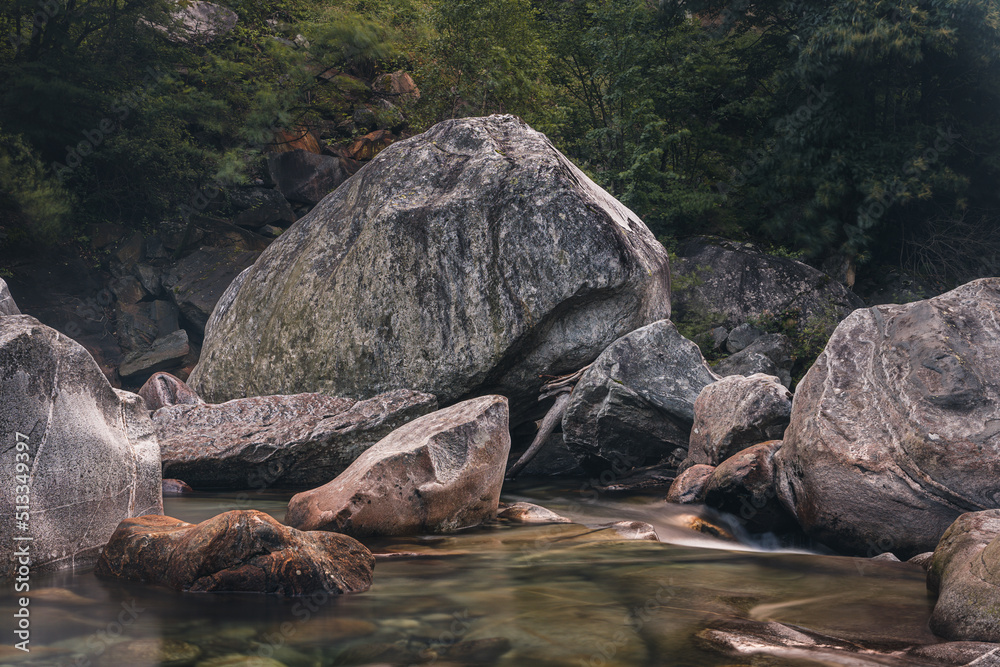 Fototapeta premium Atmosphärischer Naturhintergrund mit riesigen Steinen im Bergfluss. Große Felsen im mächtigen Wasserstrom, Nahaufnahme. Naturhintergrund mit Wald. Dunkel türkisblauer Fluss mit Steinen.