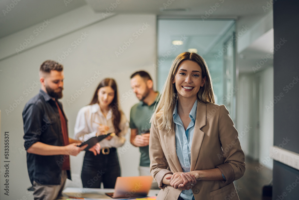 Obraz premium Businesswoman posing while having a meeting with her team in the office