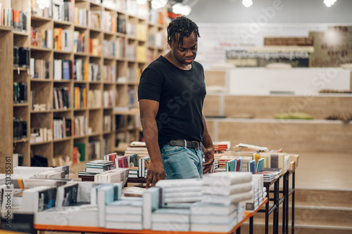 African american man picking and reading books in library or bookstore photo