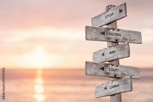 stop existing and start living text engraved on wooden signpost by the ocean during sunset.