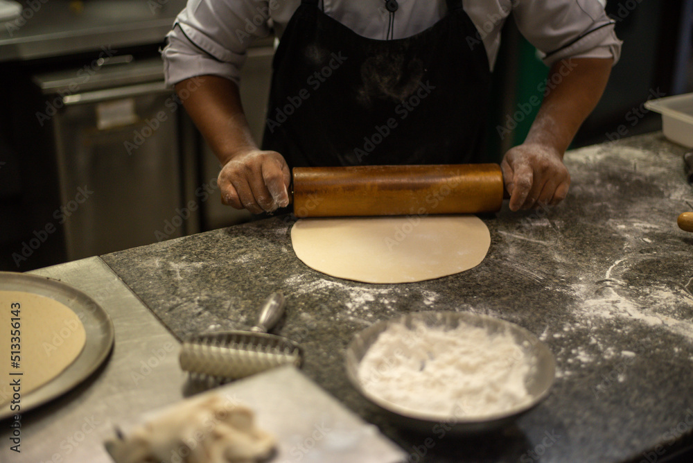 Fototapeta premium Male baker prepares bread. Male baker sprinkle the dough with flour. Making bread. Top view. Rustic style