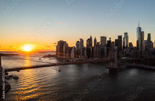 Aerial view of Brooklyn bridge and modern downtown skyscrapers against romantic sunset. Rays of sun reflecting on water surface. Manhattan  New York City  USA