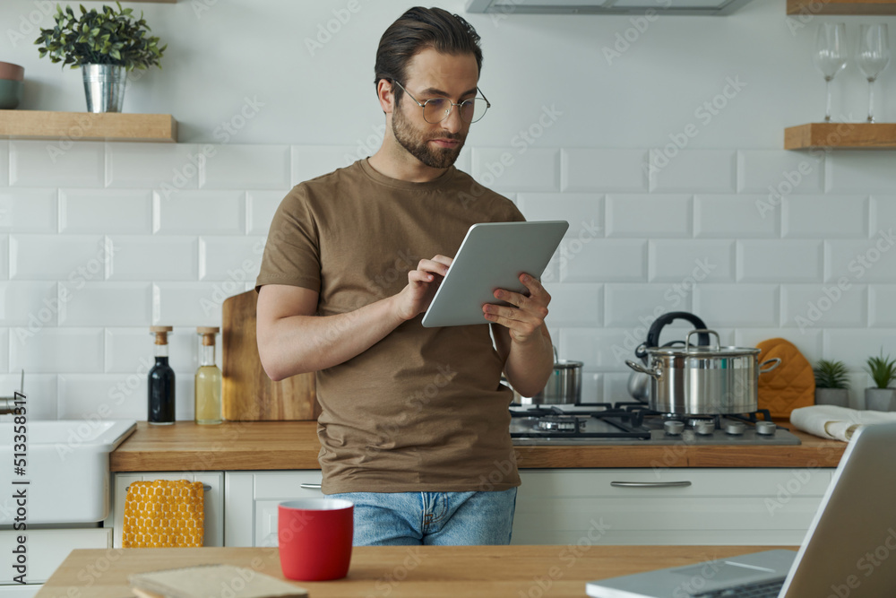Confident young man using technologies while working from domestic kitchen Confident young man using technologies while working from domestic kitchen