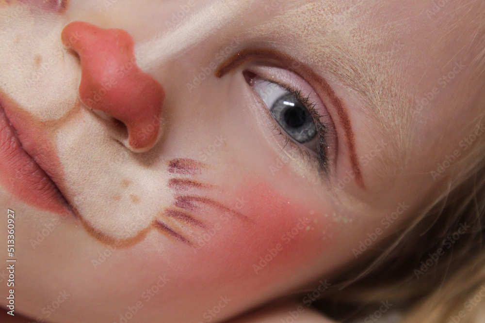 Naklejka premium A girl with blue eyes and children's makeup. A child with a funny face painting. Makeup of a rabbit on the face of a child. Children's holiday, event, birthday, easter bunny, entertainment