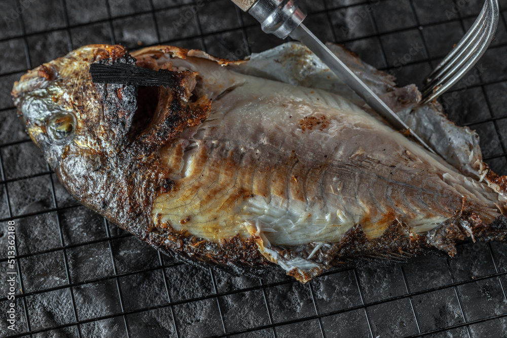Eating whole grilled Dorado or Sea Bream on dark textured background. Healthy eating concept. Seafood recipes Eating whole grilled Dorado or Sea Bream on dark textured background. Healthy eating concept. Seafood recipes