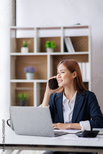 Asian businesswoman talking on phone, using laptop, looking at screen, entrepreneur manager consulting client by call, looking at computer screen, discussing project, reading information