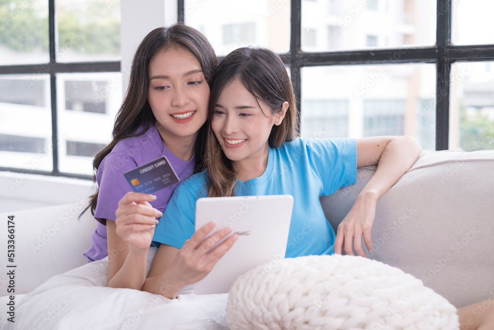 Cute Young Couple Hugging together on Sofa in the Morning. Young Couple using tablet for online Shopping. LGBTQ and Same Sex Marriage Concept. Lesbian love and romance. Cute Young Couple Hugging together on Sofa in the Morning. Young Couple using tablet for online Shopping. LGBTQ and Same Sex Marriage Concept. Lesbian love and romance.