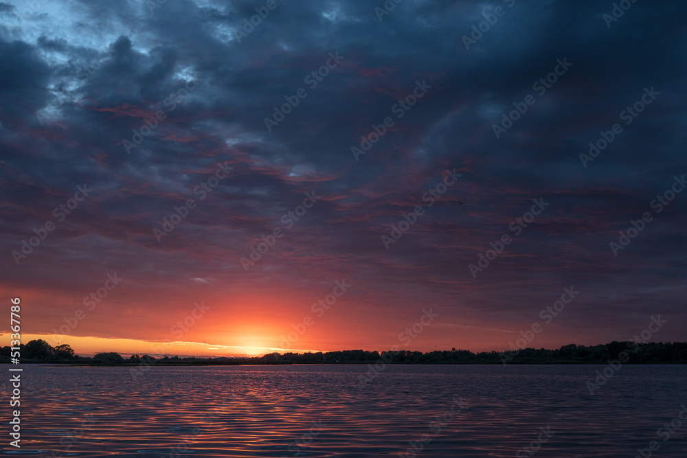 Wonderful colorful sunset on river. View of dramatic sky reflection on water and birds flying in the sky.