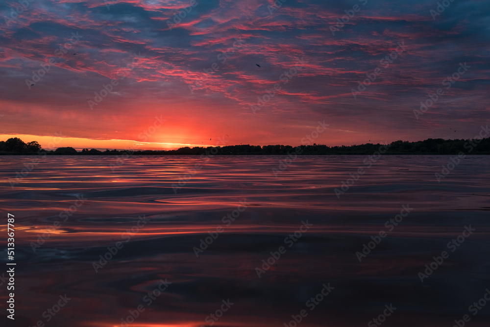 Wonderful colorful sunset on river. View of dramatic sky reflection on water and birds flying in the sky.