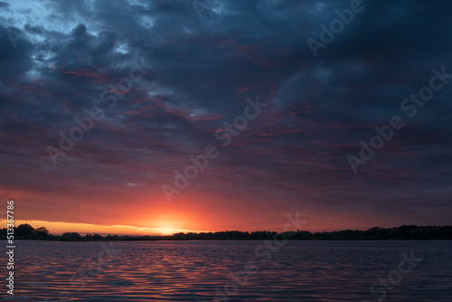 Wonderful colorful sunset on river. View of dramatic sky reflection on water and birds flying in the sky.