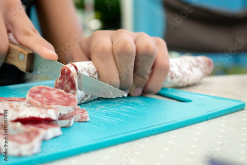 Person preparing and cutting meat (fuet) with a knife on a board. (Pica pica)
camping and summer. photo