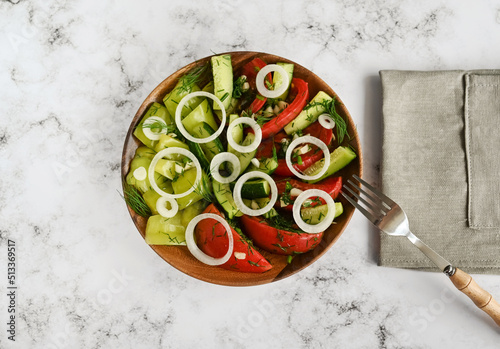 Salad consisting of fermented vegetables: tomatoes, cucumbers and bell peppers in a wooden plate on the marble table, a fork with a napkin, a copy space. 