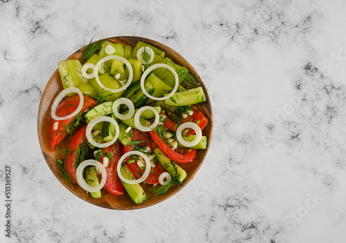 Fermented chopped natural vegetables: tomatoes, cucumbers and bell peppers in a wooden plate on the marble table, a copy space