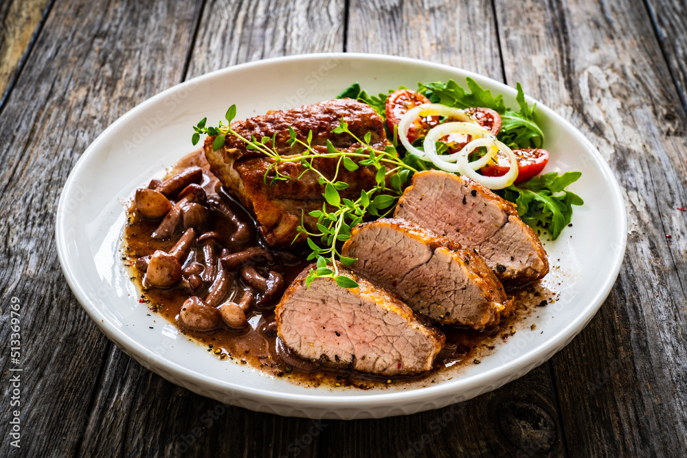Roasted pork loin with shimeji mushrooms in sauce, fresh thyme, greens and cherry tomatoes on wooden table
Roasted pork loin with shimeji mushrooms in sauce, fresh thyme, greens and cherry tomatoes on wooden table