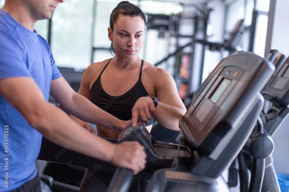 Young female personal trainer setting treadmill to client Young female personal trainer setting treadmill to client