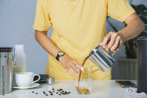 Fotobehang person using pitcher Pour brewed coffee and brew cold black coffee on a mug with roasted Arabica beans on a white table and coffee maker