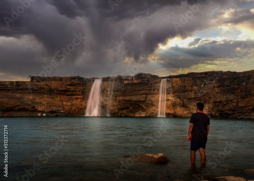 Man standing facing a waterfall