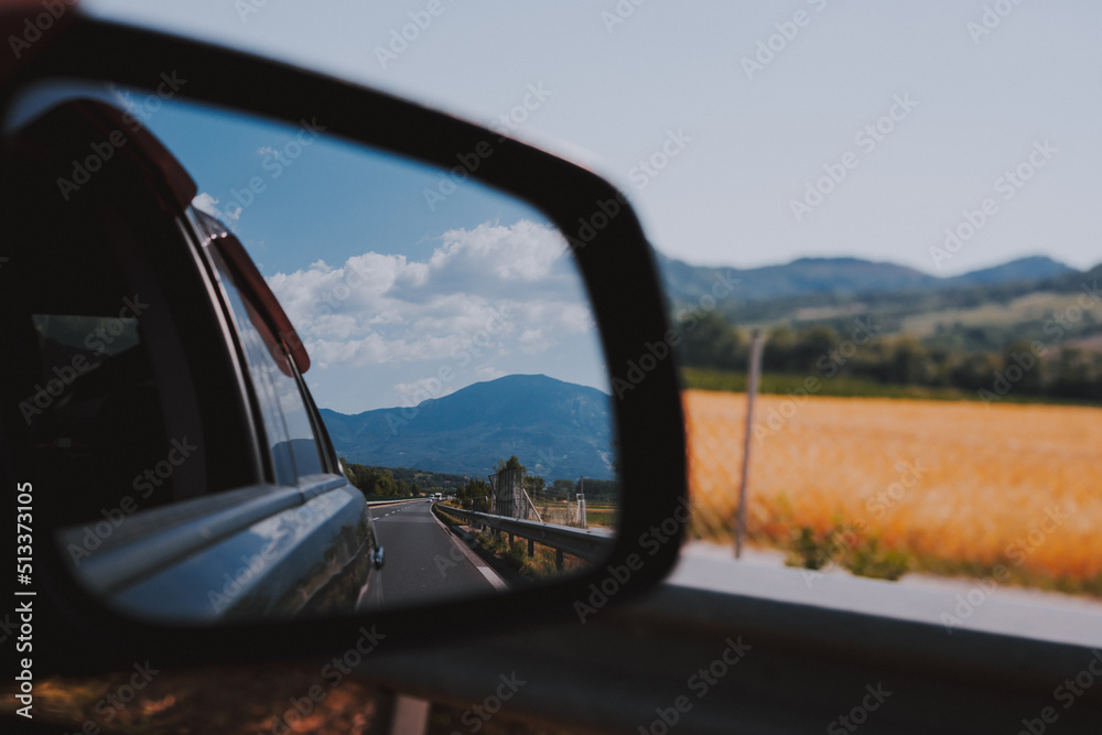Car rear view mirror. Road, field and mountain reflection in mirror. Traveling in Europe