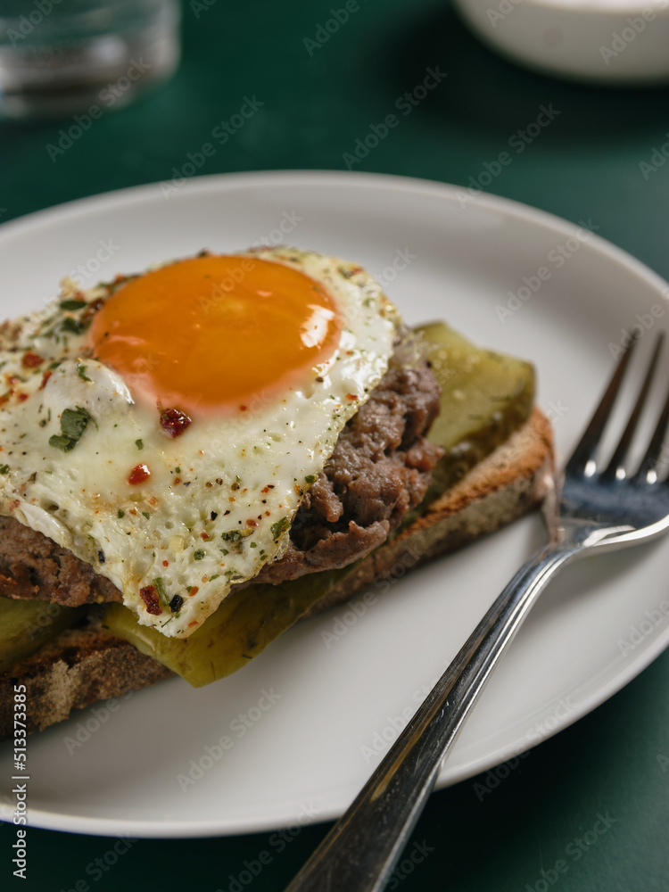 Beefsteak with fried egg on a slice of bread with pickled cucumbers