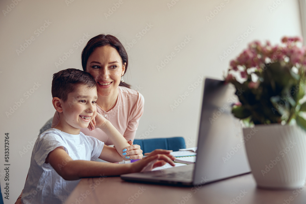 Small cute schoolboy with braces using laptop in online learning, happy mother smiling. Small cute schoolboy with braces using laptop in online learning, happy mother smiling.