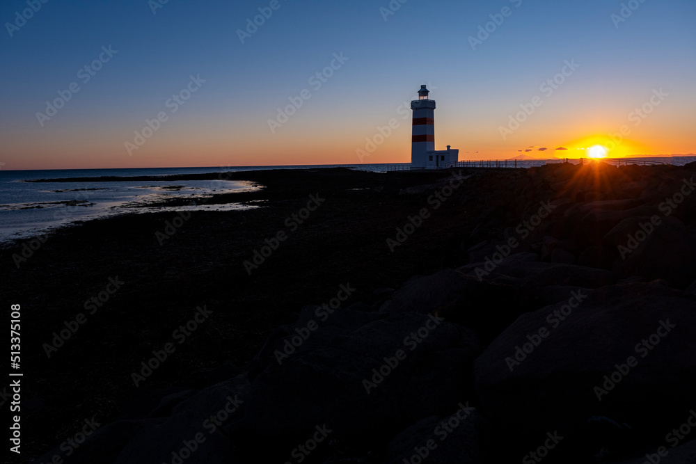 Beautiful view of white and red colored old lighthouse Garður on the coast of Suðurnesjabær on Reykjanes peninsula, Iceland with beach during midnight sun
