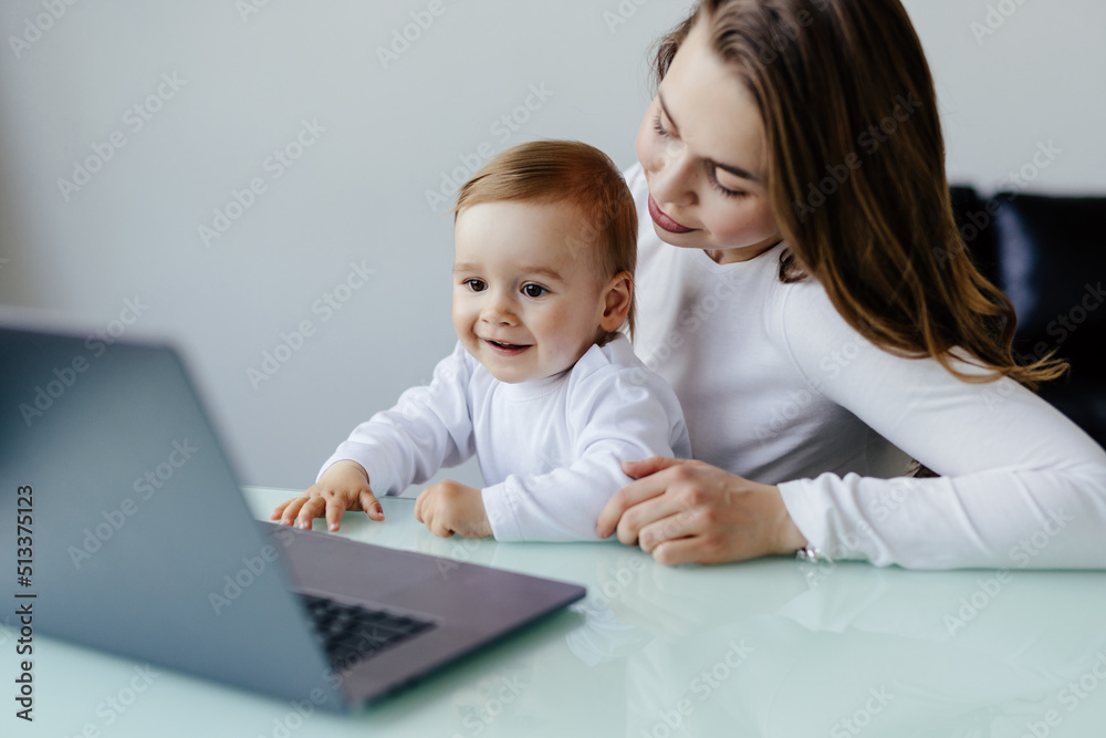 Young beautiful woman multitasking, working from home teaching two year old son to draw. Woman spending quality time with her toddler child. Homeschooling concept. Young beautiful woman multitasking, working from home teaching two year old son to draw. Woman spending quality time with her toddler child. Homeschooling concept.