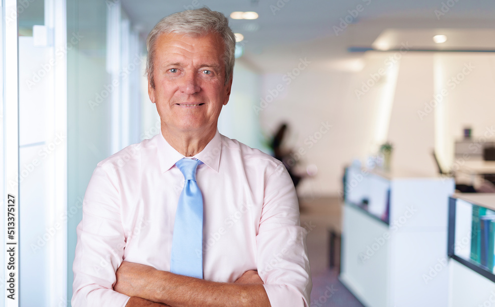 Executive grey haired businessman standing with arms crossed at the office