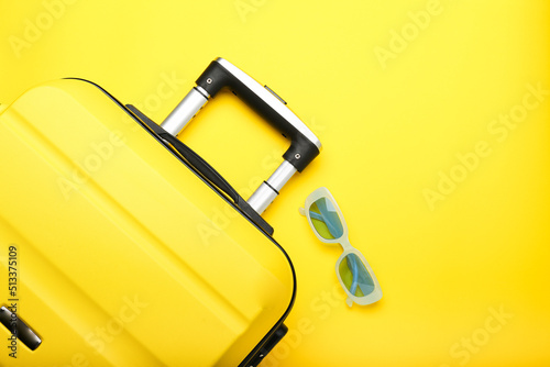 yellow suitcase and blue sunglasses on a yellow background. Top view, summer concept